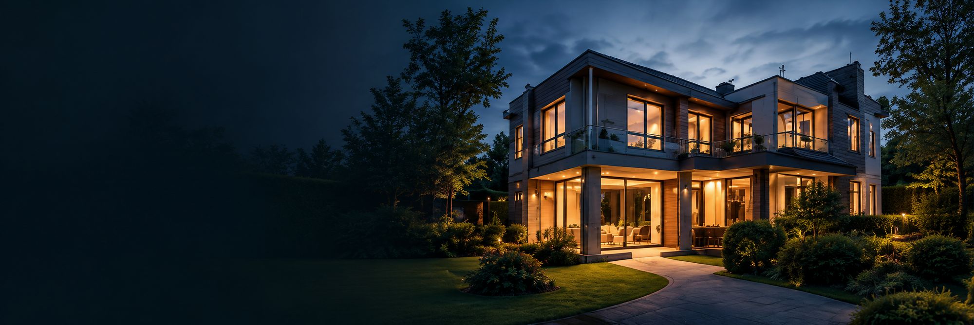 Vrijstaande woning in de avond met verlichte ramen en gevelverlichting.
